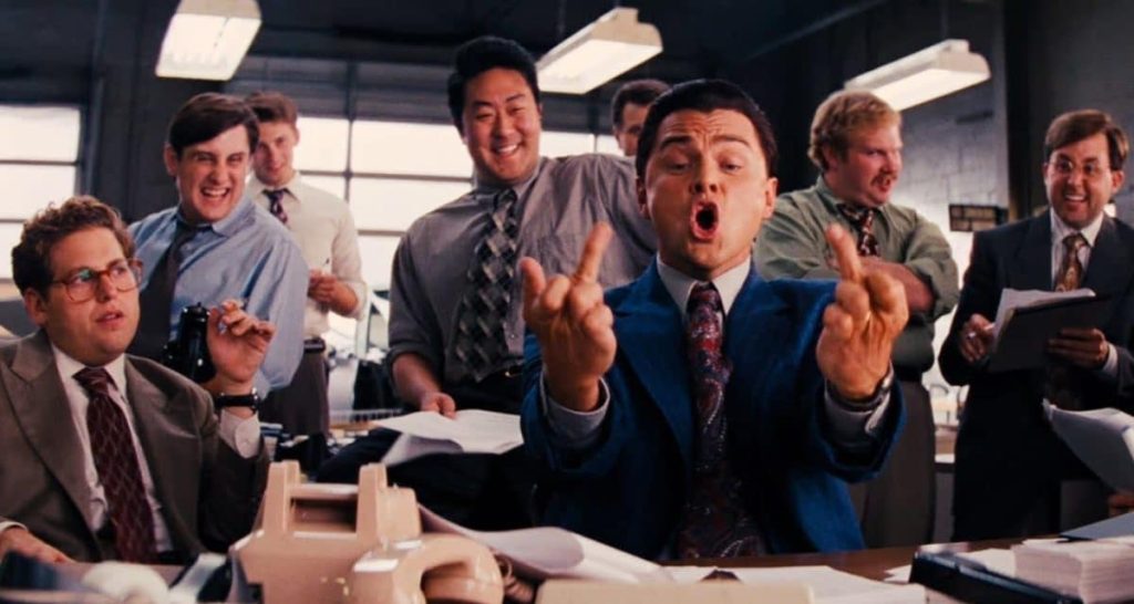 Scene from a movie showing a man in a suit shouting and gesturing, surrounded by colleagues celebrating in an office